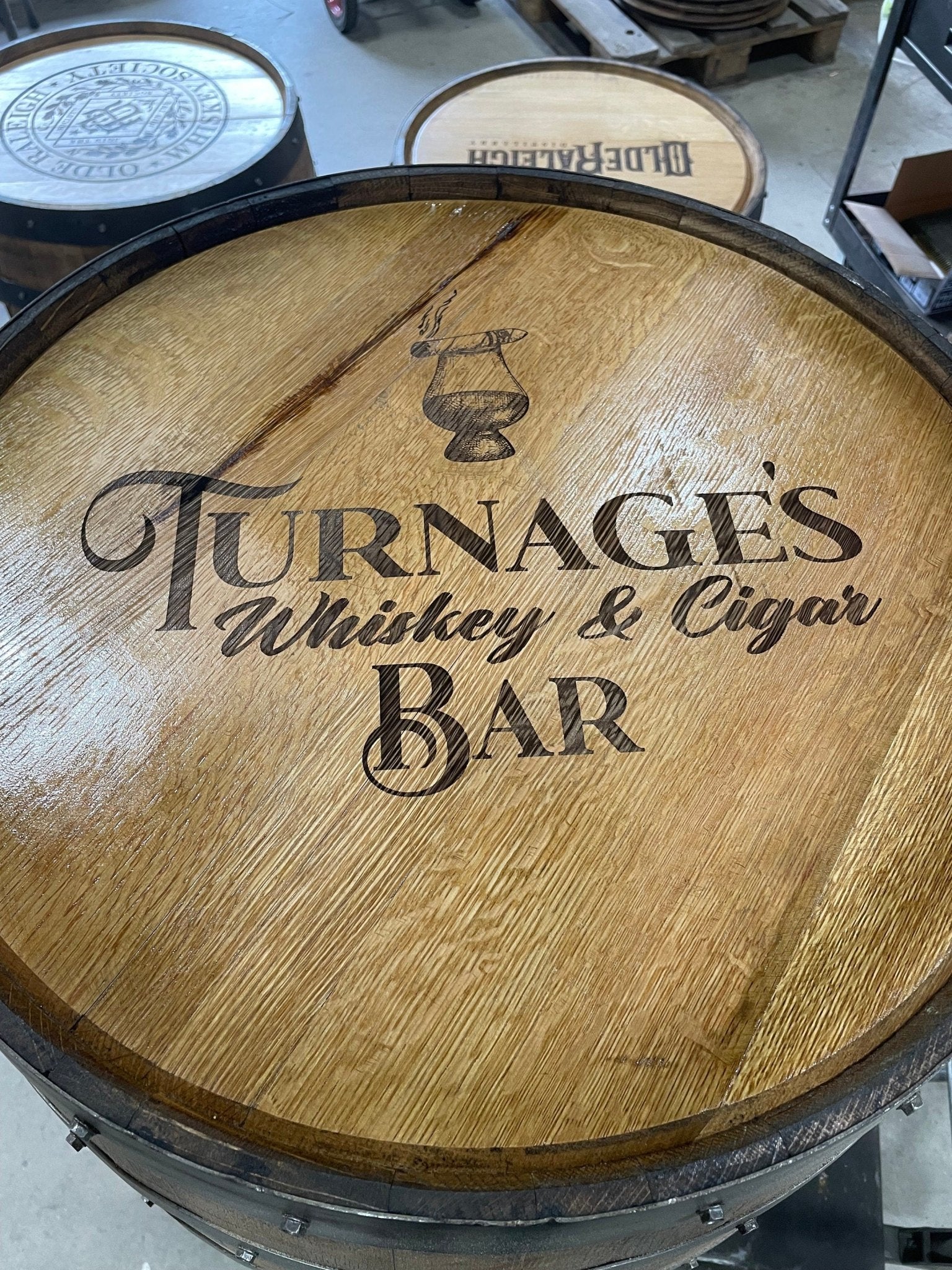 Custom bourbon barrel table featuring laser engraved whiskey and cigar bar artwork on hand sanded clear coated oak barrel head