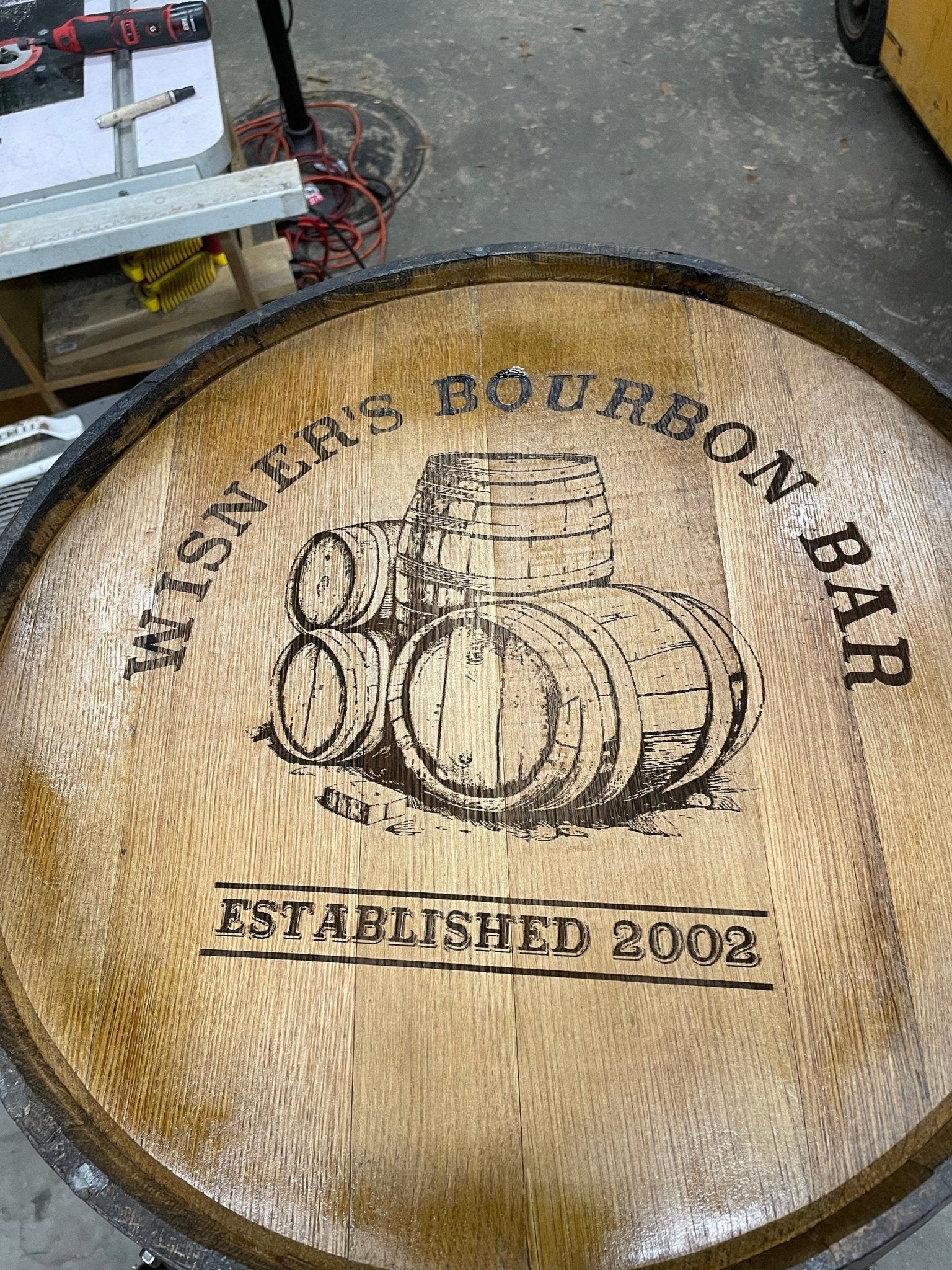 Bespoke bourbon barrel table displaying custom laser etched distillery crest graphics on authentic spirit aged oak timber top