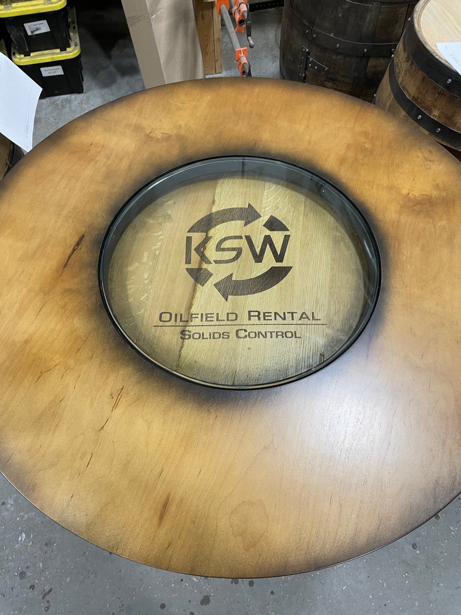 Custom bourbon barrel table showcasing precision laser engraved barrel head logo under heavy protective clear glass inset