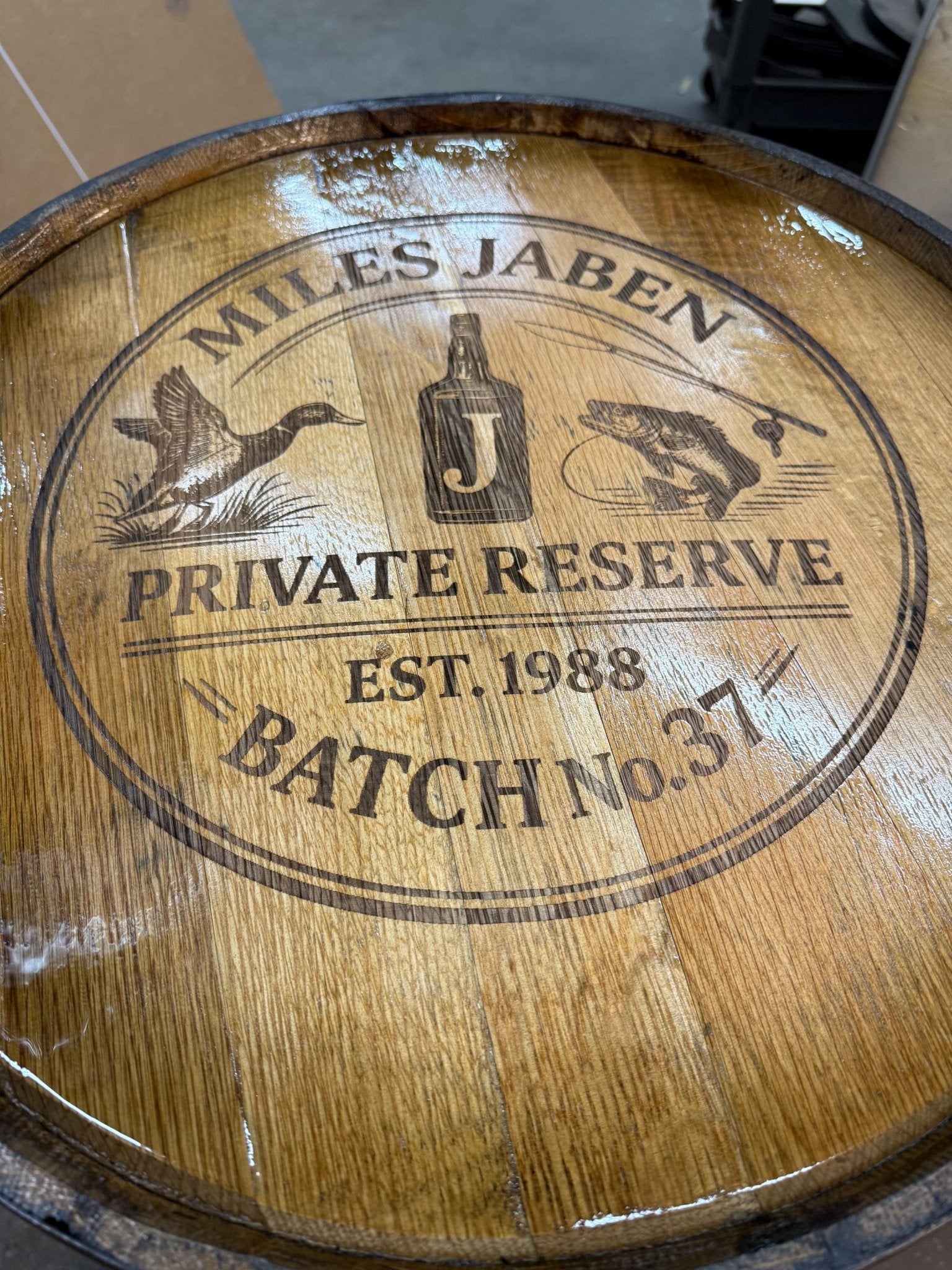 Custom bourbon barrel table displaying bespoke laser engraved private reserve batch graphics on clear coated oak barrel plaque