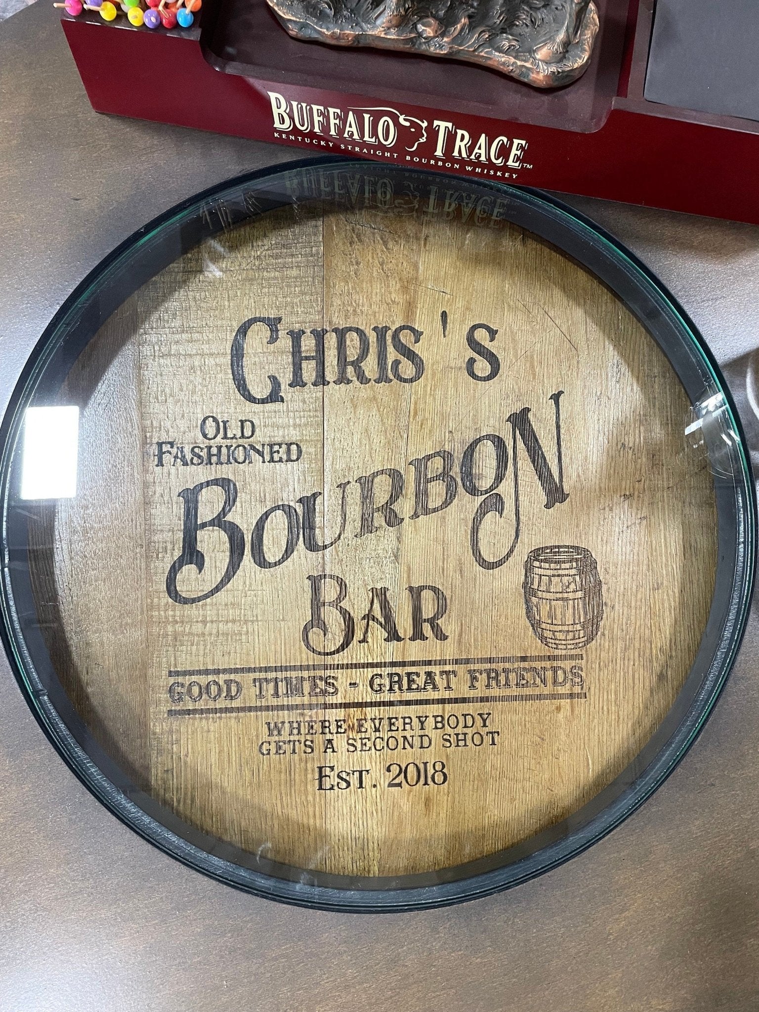 Custom bourbon barrel table designed with protective glass surface revealing personalized laser etched oak barrel head plaque